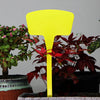A bright yellow T-shaped plant marker is shown standing in a pot among dark red and green foliage.