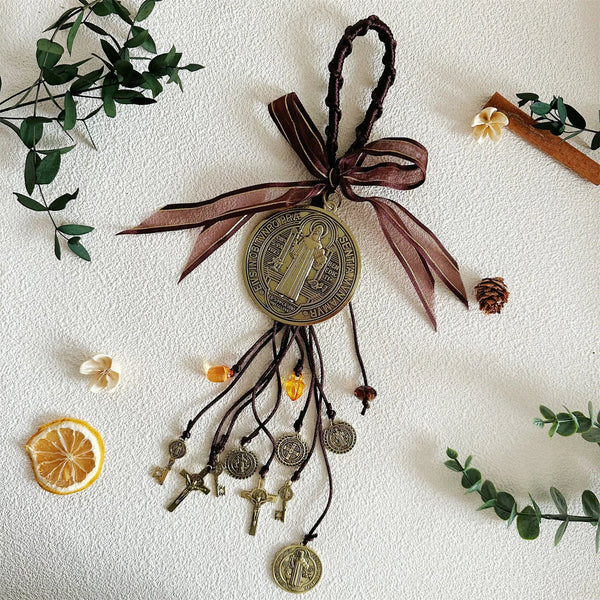 Antique silver Saint Benedict medal charm hanging from a dark ribbon with olive leaves and small charms