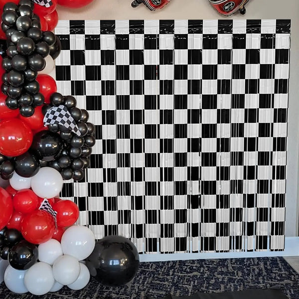 A black and white checkered foil curtain backdrop decorated with red, black, and white balloons.