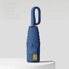 A blue compact folding umbrella with a handle and protective sleeve is shown against a light gray background.