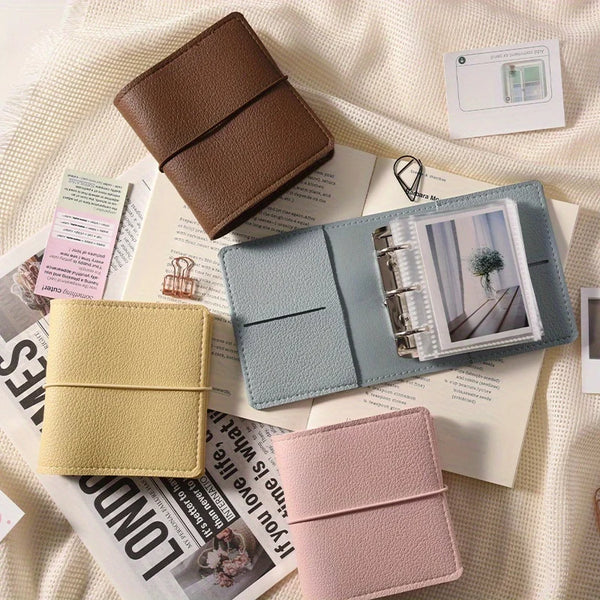 Un mini album photo en faux cuir bleu clair et rose est exposé sur un fond blanc avec des papiers.