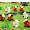 A collection of resin highland cow figurines in white and orange colors displayed on a green textured surface.