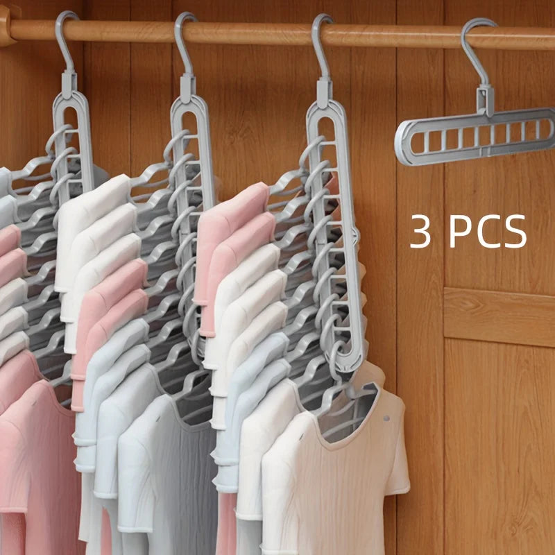 A set of three foldable plastic hangers in various shades of pink, white, and gray hanging on a wooden rod.