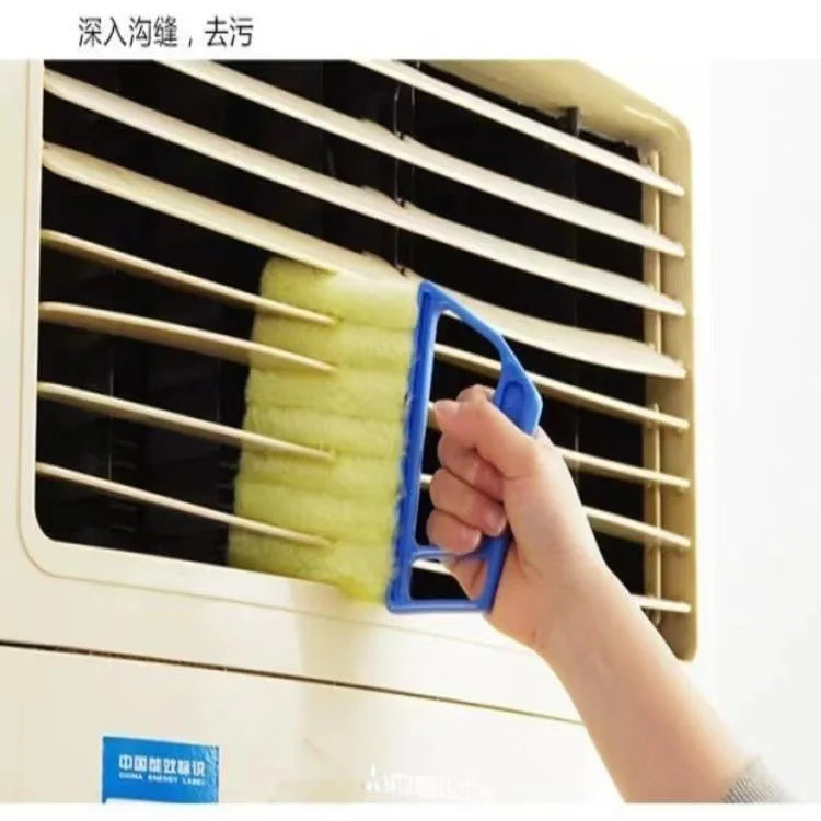 A hand is using a blue multi-functional cleaning brush to clean the slats of a window blind.