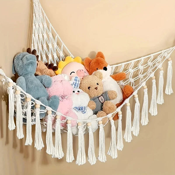 A white net hammock features various soft plush animals hanging from it against a beige wall.