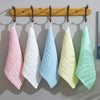 Un set de cinco toallitas orgánicas de algodón para bebé y cara colgadas en una percha de madera en colores pastel.