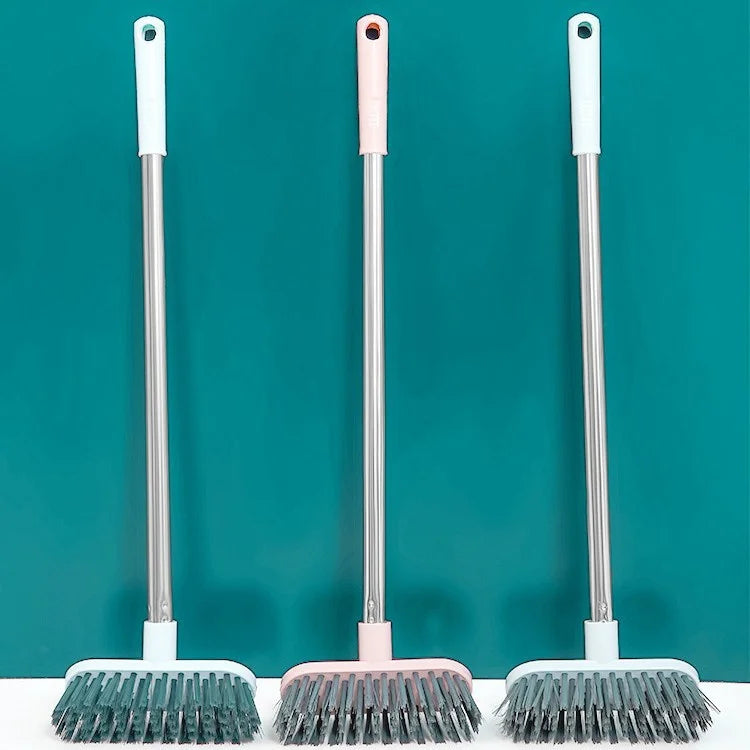 Three long-handle floor scrub brushes with silver and pink handles and grey bristles against a teal background.