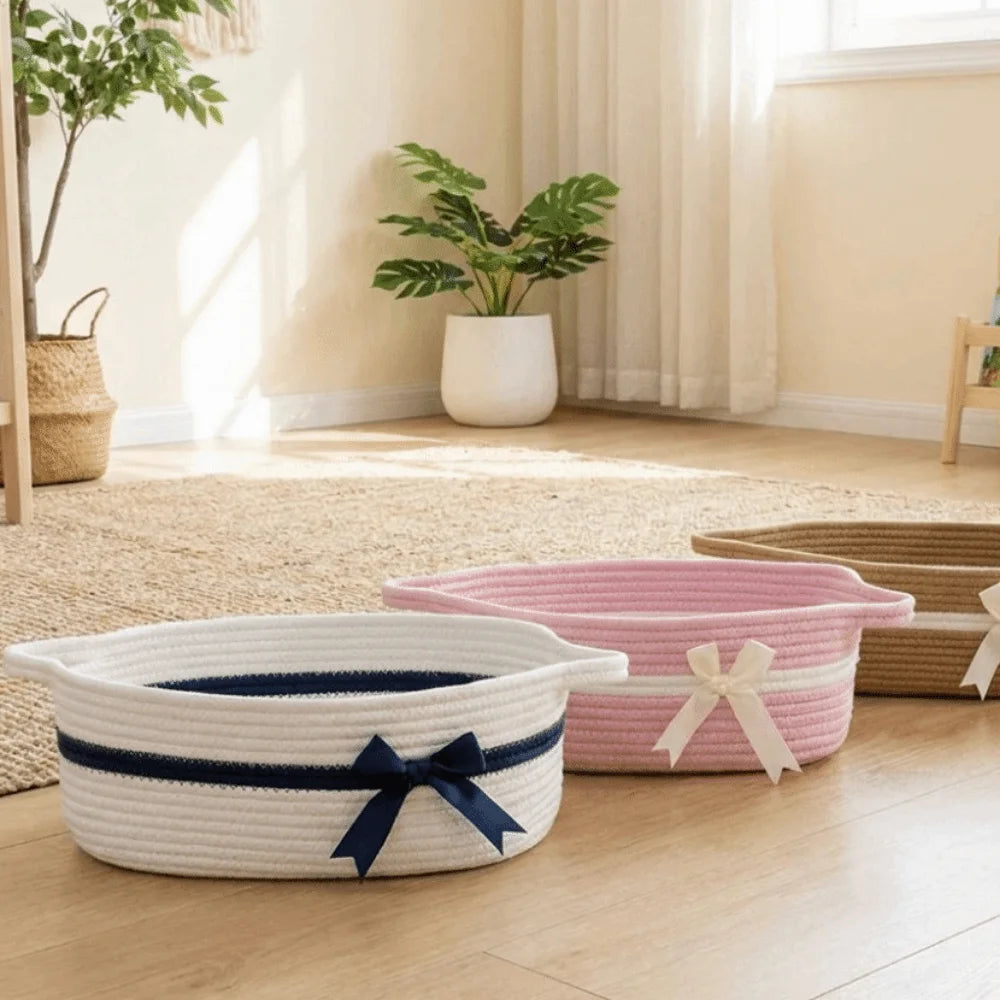 A white woven cotton rope storage basket tied with a navy blue ribbon sits on a light wood floor.