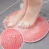 A close-up of a pink reusable silicone foot scrub brush being used on a person's foot.