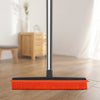 A silver adjustable rubber broom with an orange head rests on a wooden floor.