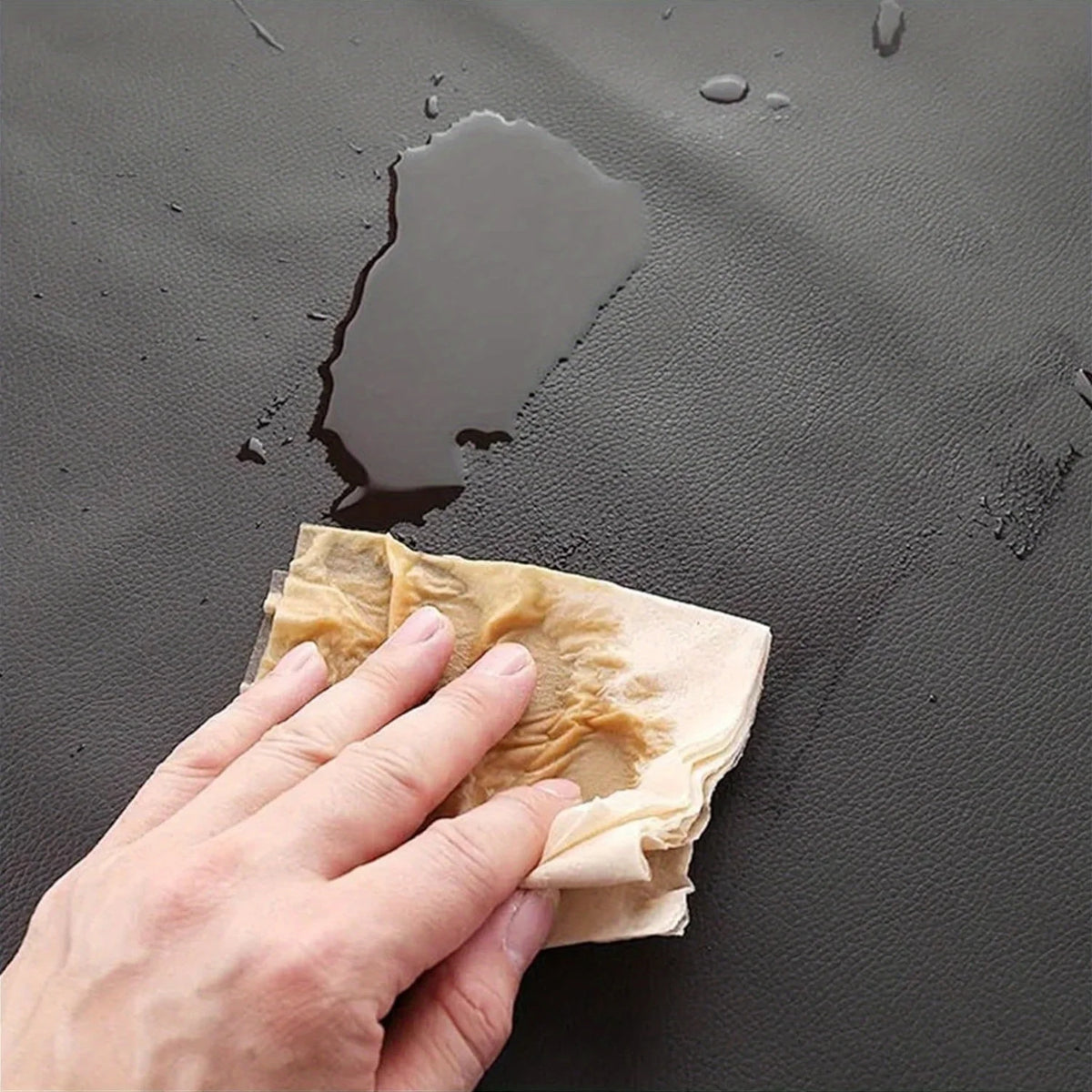 A hand is holding a piece of tan PU leather material on a dark surface, demonstrating the texture and flexibility of the apro