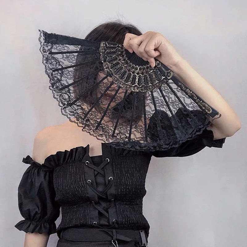 A woman holds a black lace fabric folding hand fan with intricate detailing against a light gray background.