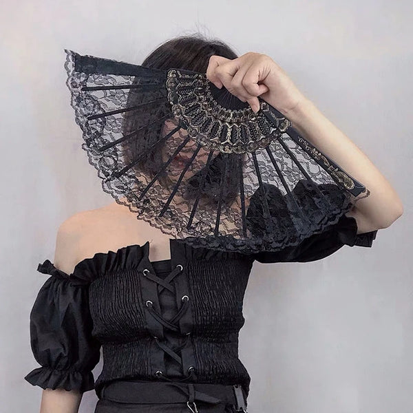 A woman holds a black lace fabric folding hand fan with intricate detailing against a light gray background.