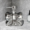 A chrome ceramic pump dispenser bottle with a bowknot design sits on a light surface.