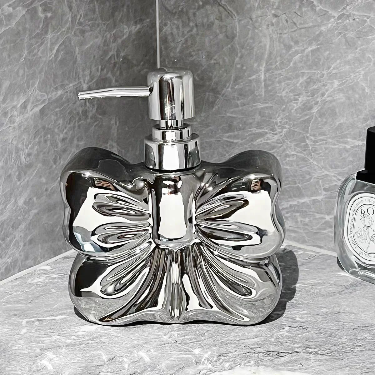 A chrome ceramic pump dispenser bottle with a bowknot design sits on a light surface.