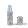 A silver glass perfume spray bottle with a silver cap and a loose, glittery diamond-like product.