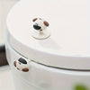 A white toilet seat lifter handle shaped like a cartoon dog is visible on the toilet tank.