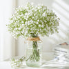 A bouquet of artificial baby's breath flowers in a glass jar with twine tied around the stems.