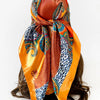 A square paisley print scarf in shades of orange, blue, and rust fabric tied around a dark hair.