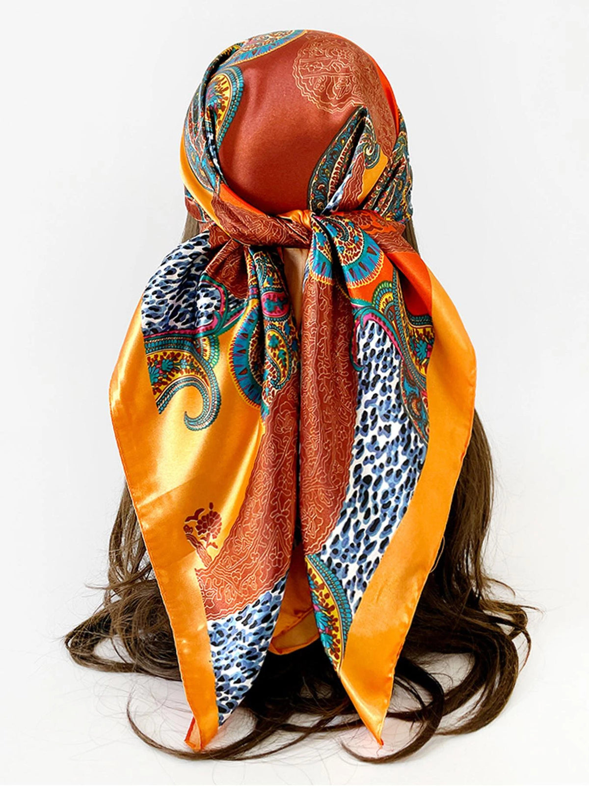 A square paisley print scarf in shades of orange, blue, and rust fabric tied around a dark hair.