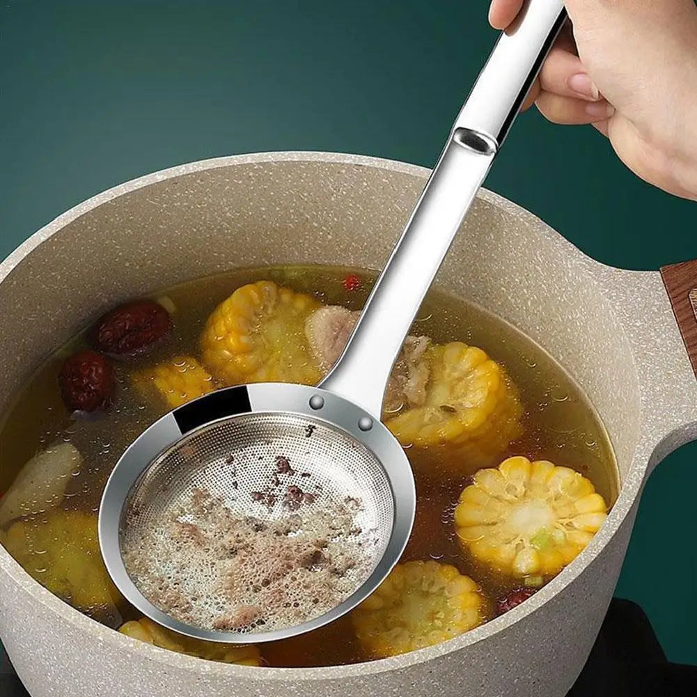 A hand is using a stainless steel fat skimmer strainer to remove fat from soup in a pot.