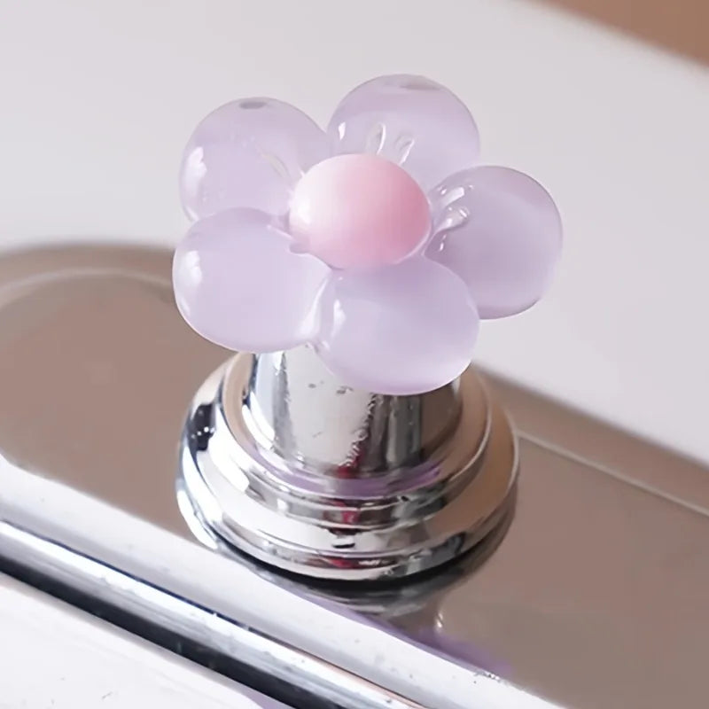 A flower-shaped toilet flush button with translucent pink and white petals resting on a chrome fixture.