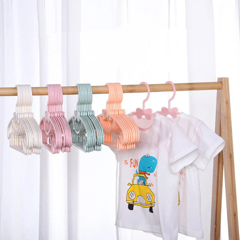 A wooden clothes rack displaying several pink, green, and orange plastic hangers for children's clothing.
