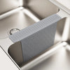 A gray silicone kitchen sink protector mat with drainage features is shown inside a stainless steel sink.