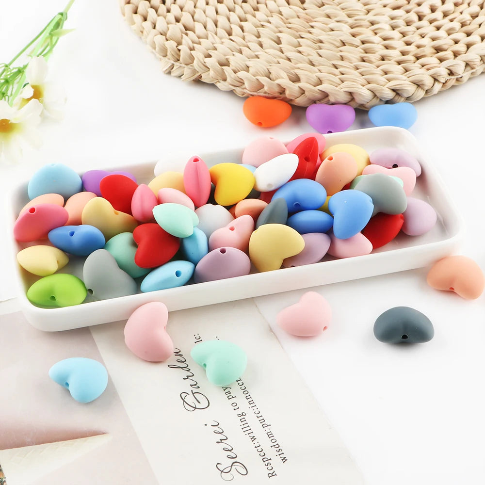 A collection of 10 colorful silicone heart charm beads in various shades of pink, yellow, blue, and red arranged on a white t