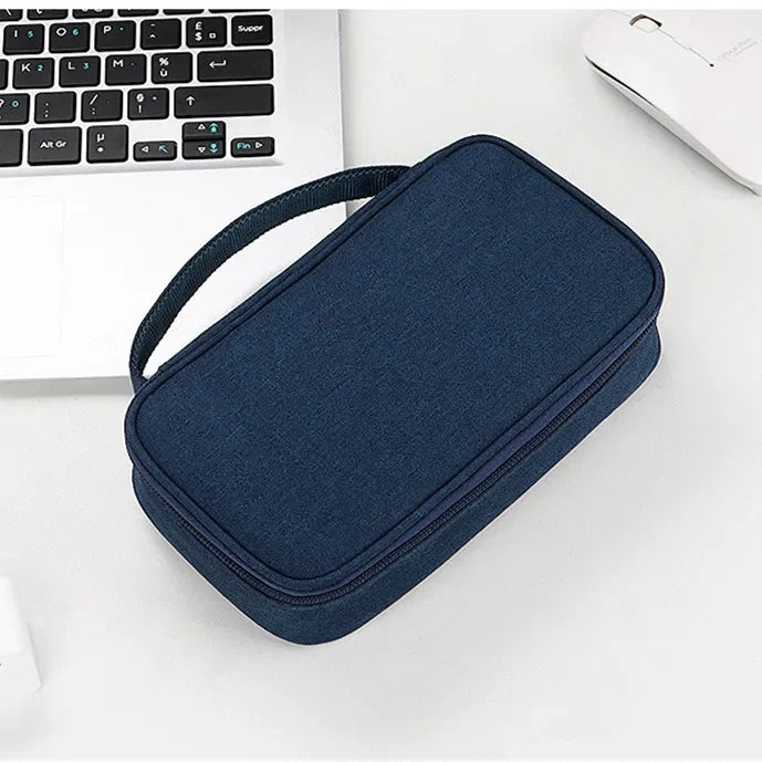 A dark blue multi-purpose travel electronics organizer bag resting on a white surface next to a laptop and mouse.