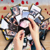 Hände montieren eine DIY Fotoalbumbox mit Fotos und Dekorationen auf einer Holzoberfläche.