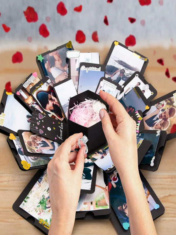 Hands are assembling a DIY photo album box with various photos and decorative elements on a wooden surface.
