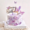 A white birthday cake decorated with purple and lavender butterfly accents on a white platter.