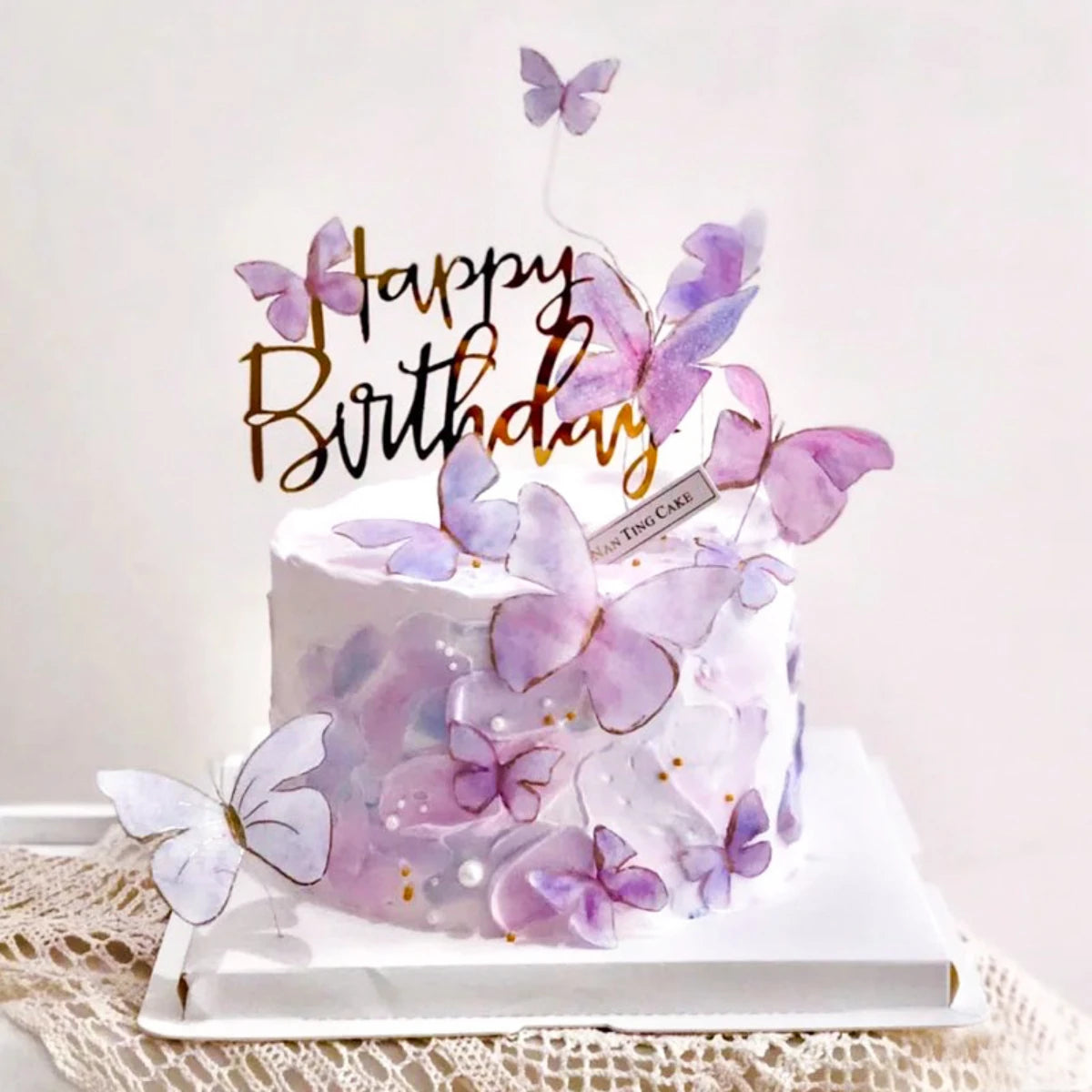 A white birthday cake decorated with purple and lavender butterfly accents on a white platter.