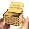 An antique wooden hand crank music box with a lid showing the inscription you are my sunshine is held in a hand.