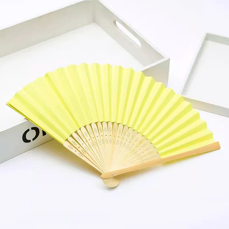 Un éventail pliable jaune vif fait de bambou et de papier, ouvert.