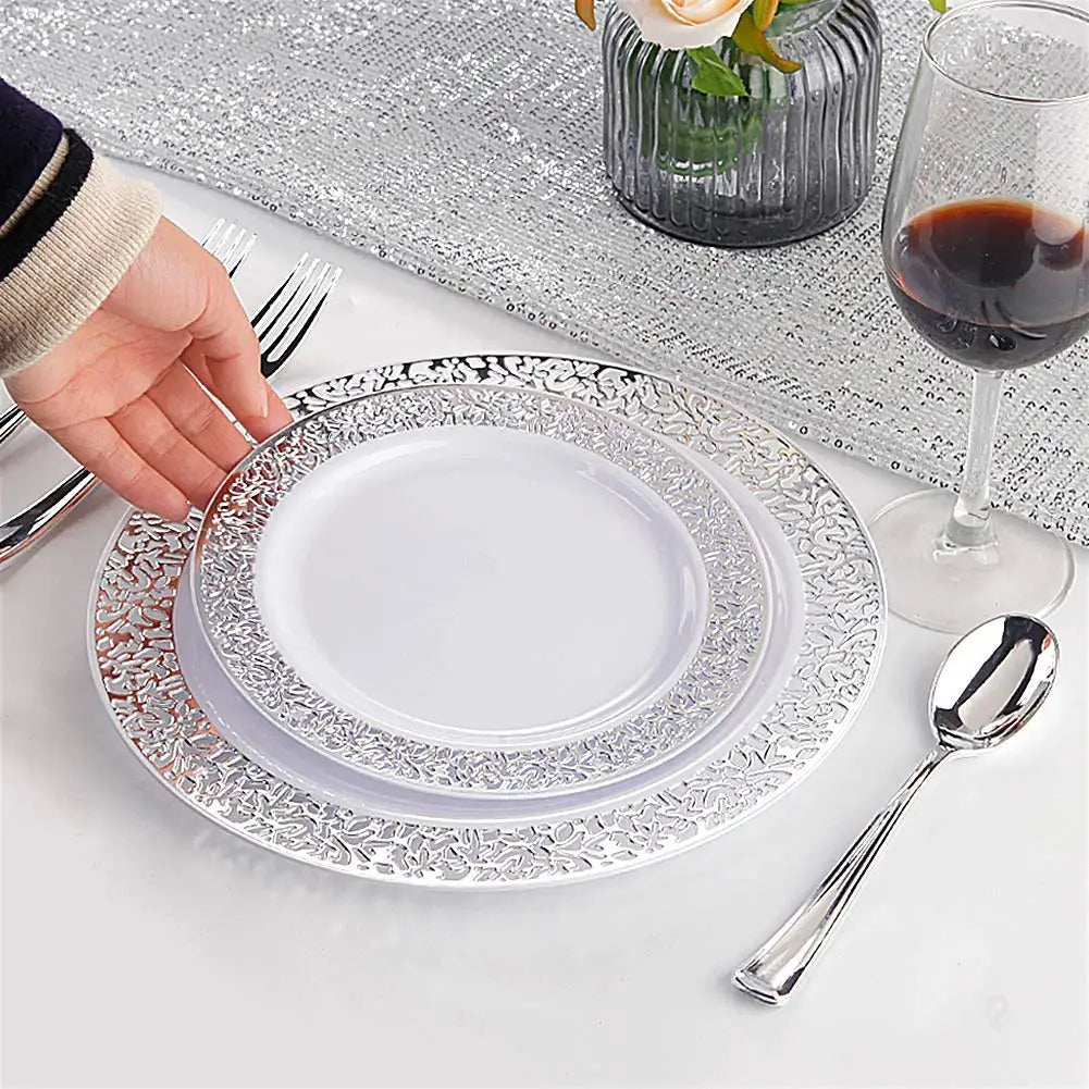Stapel dekorativer Einwegpartyteller mit silberner Spitze, Gabel und Löffel auf weißem Tisch.