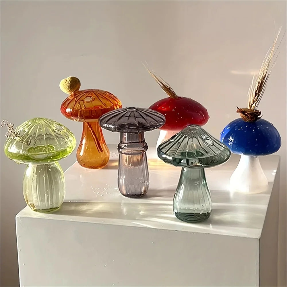A collection of glass mushroom vases in various colors including orange, red, purple, and blue, displayed on a white surface.
