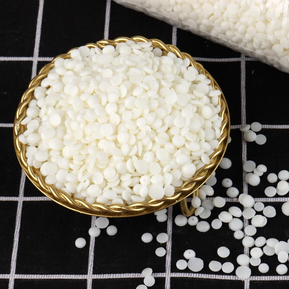 Un cuenco dorado lleno de cuentas de cera de soja blancas y esféricas sobre una superficie a cuadros blanco y negro.
