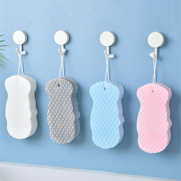 Four colorful exfoliating bath sponges shaped like fish scales hanging on a light blue wall.