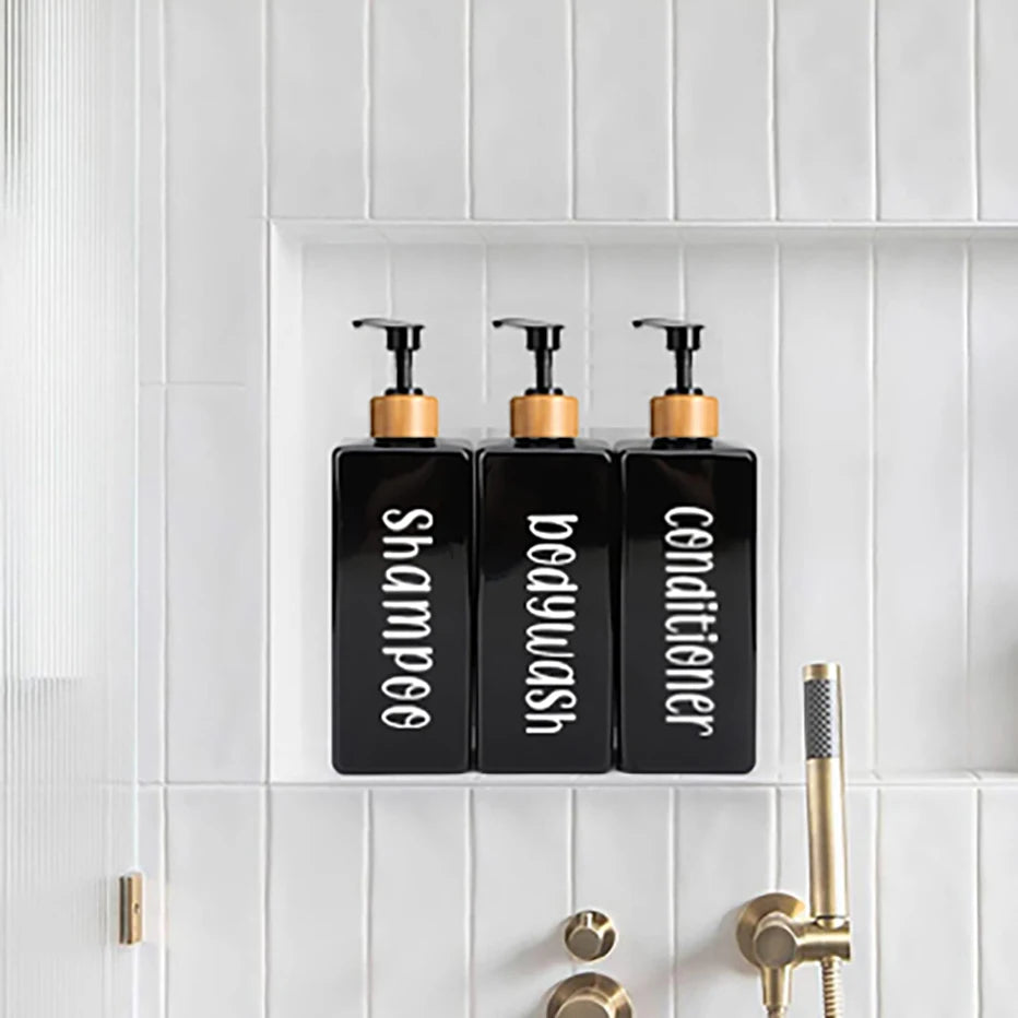 Three black pump bottles for shampoo, bodywash, and conditioner displayed on a white tiled shelf.