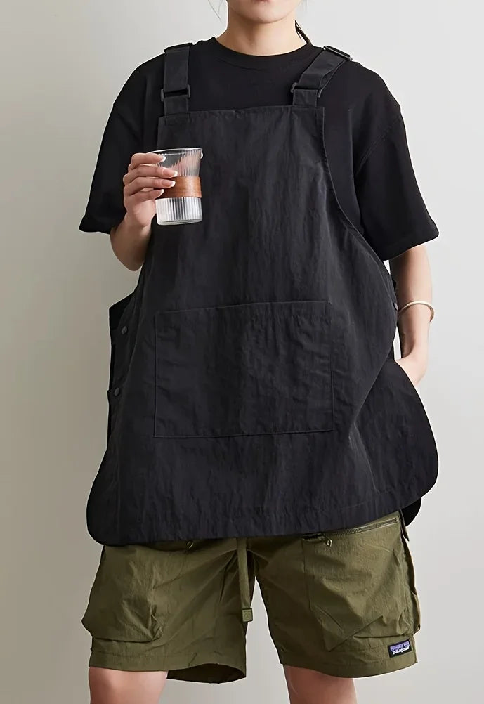 A person wearing a black waterproof outdoor work apron over a black shirt and olive green shorts.