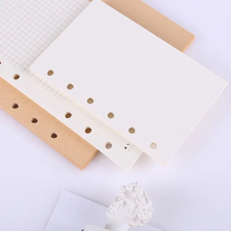 A white loose leaf notebook refill paper with perforated edges and holes for spiral binders is shown next to a brown cardboar