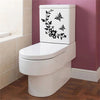 A white toilet with a black botanical leaf wall sticker on the tank, set against a pink wall.