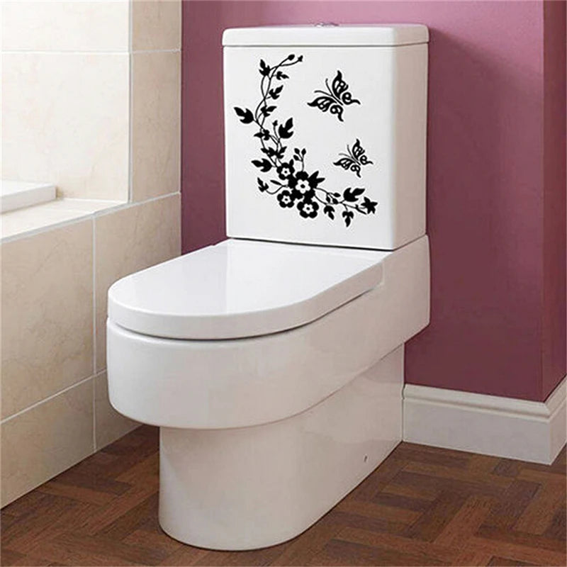 A white toilet with a black botanical leaf wall sticker on the tank, set against a pink wall.