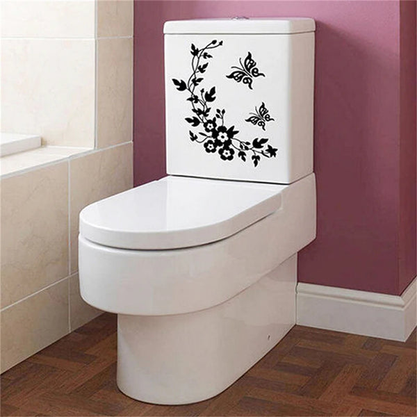 A white toilet with a black botanical leaf wall sticker on the tank, set against a pink wall.