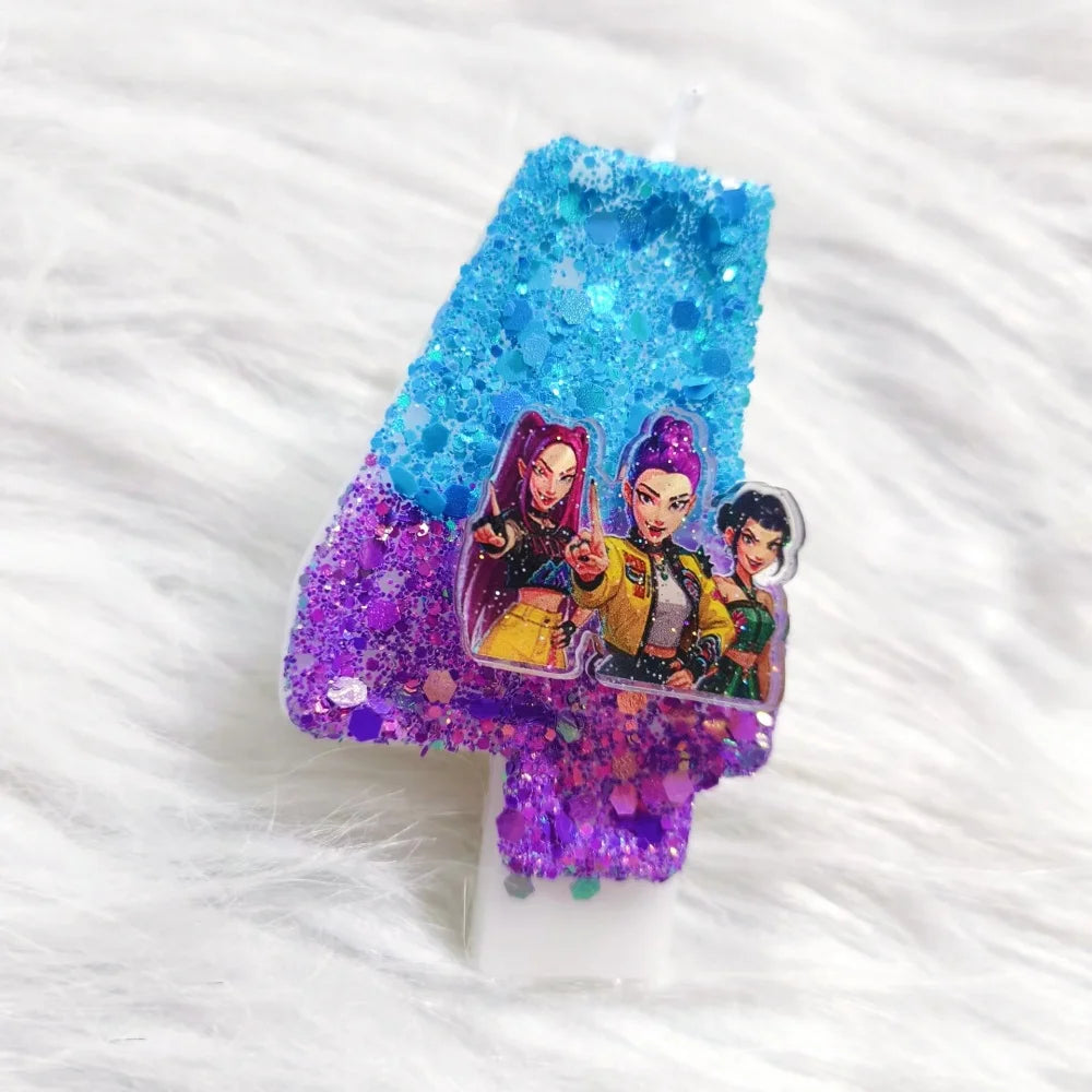 A clear candle with blue and purple glitter is decorated with a sticker featuring three female characters.