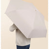 A person holding a white compact 5-fold travel umbrella against a light background.