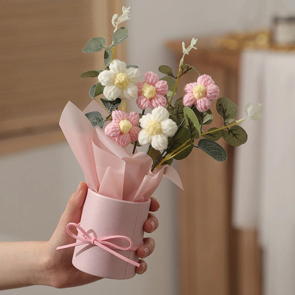 A hand holds a bouquet of artificial yarn flowers in a pink paper wrapping for home decor