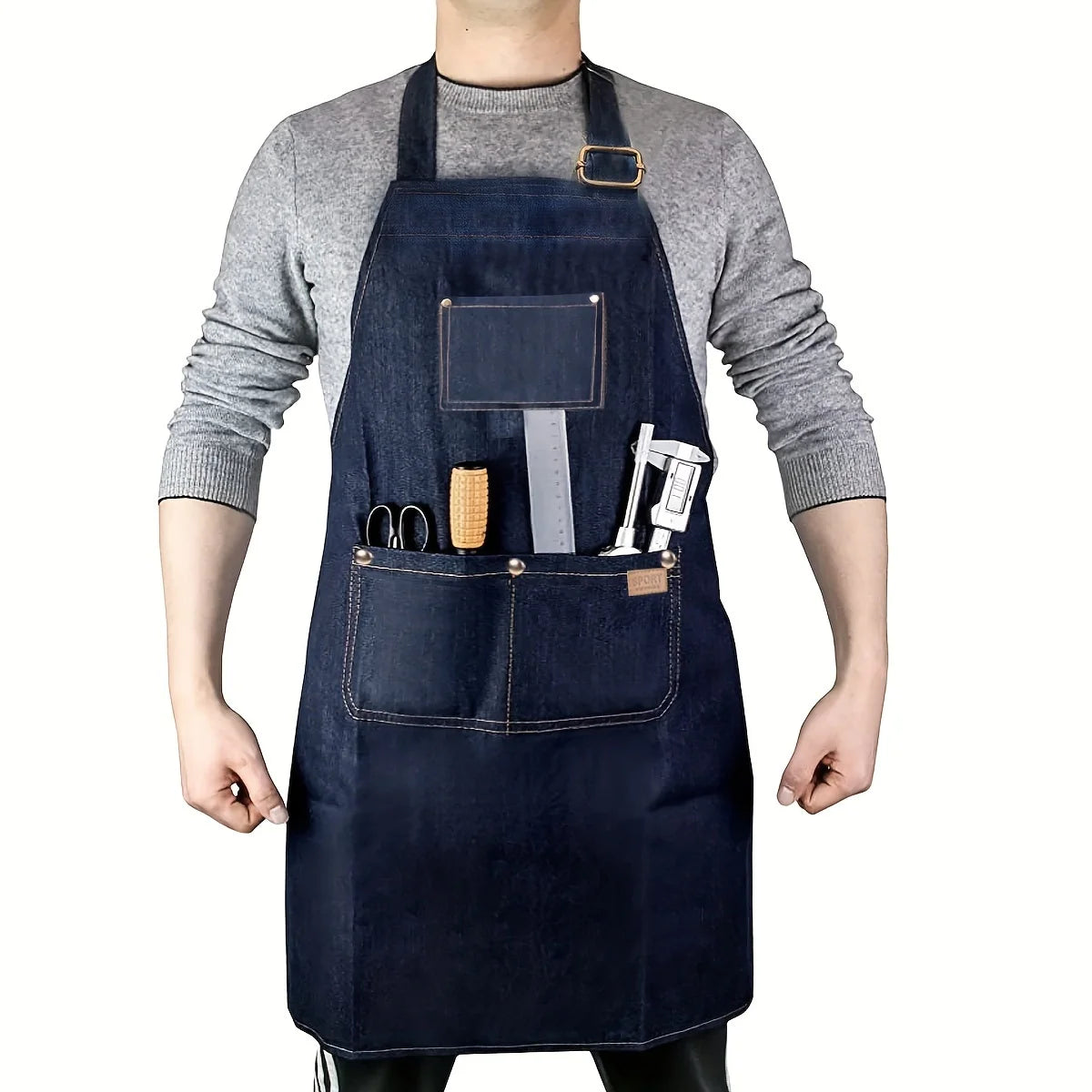 A person wearing a dark blue denim tool apron with multiple pockets and a leather strap on a gray sweater.
